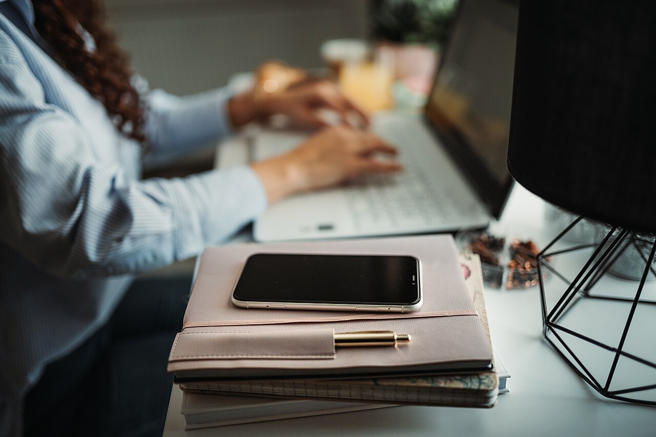 Focused individual working on a laptop at a desk with a planner and smartphone in a cozy indoor setting