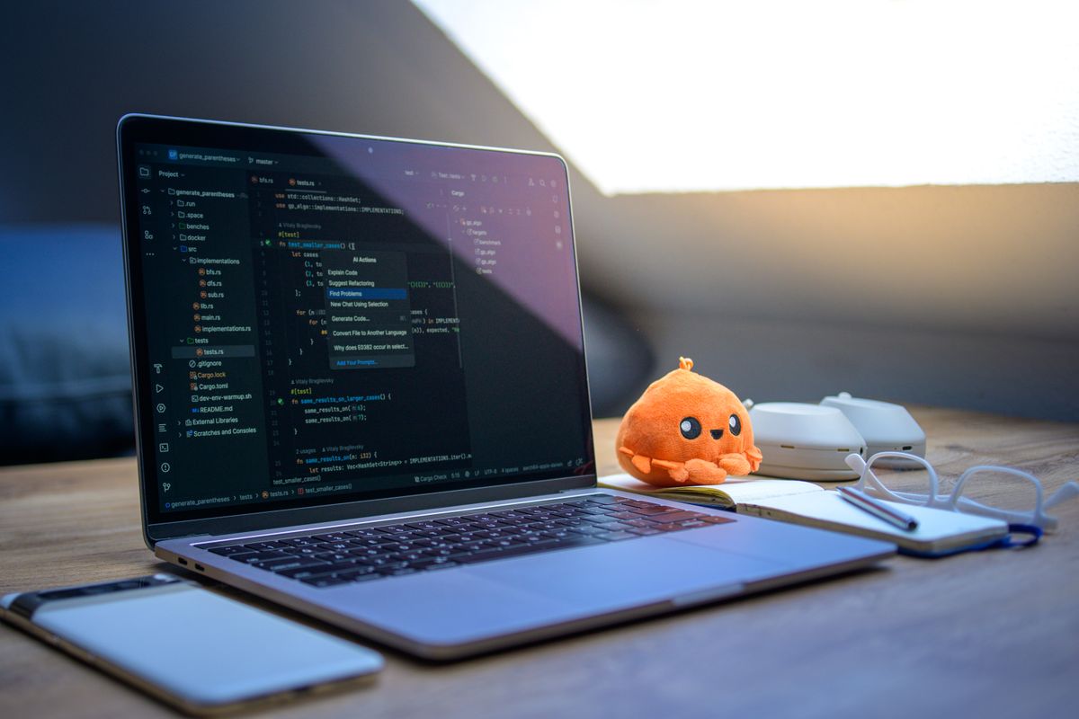 A cozy workspace featuring a laptop displaying code, a smartphone, and a cute orange plush toy on the desk.